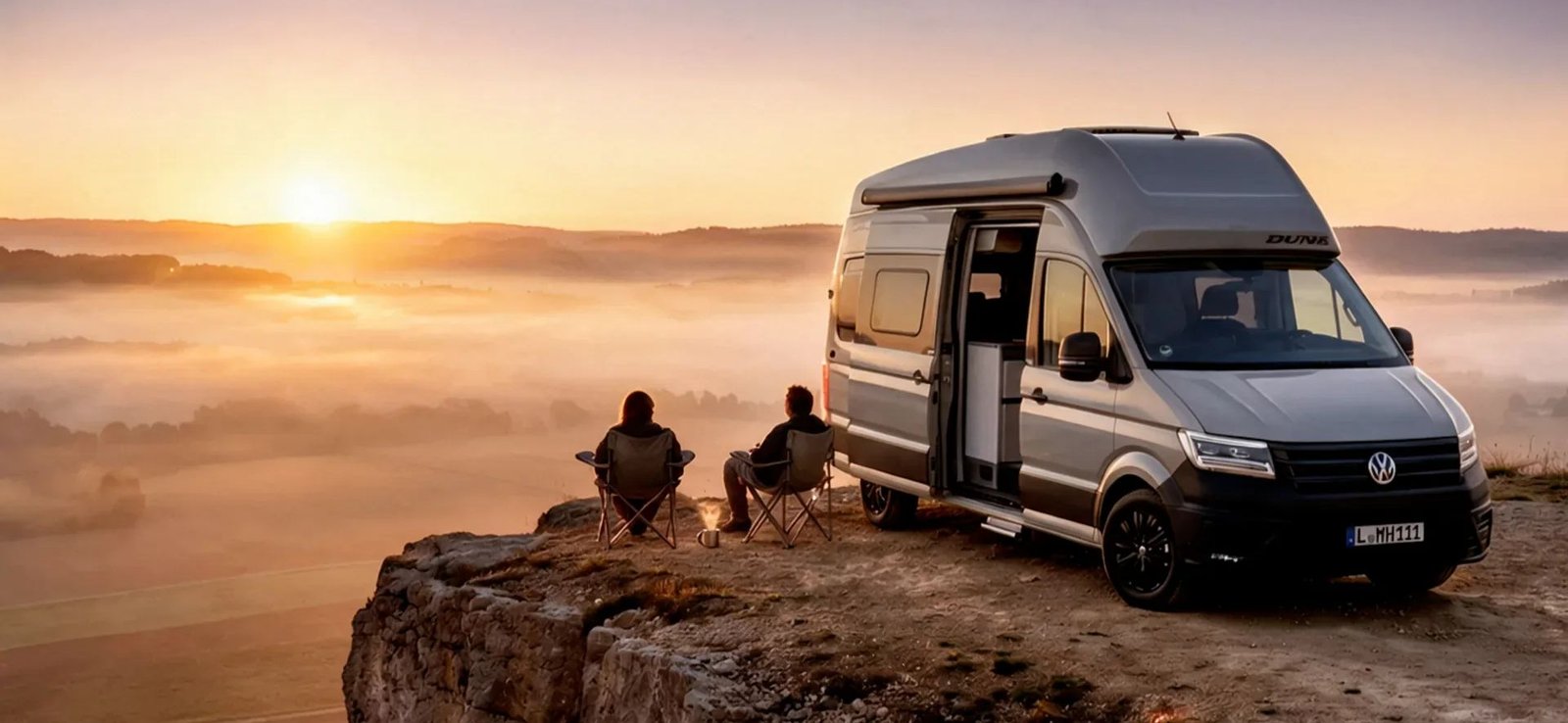 VW Grand California 600 4MOTION Sondermodell DUNE bei Sonnenaufgang auf einem Felsplateau, ein Paar sitzt davor am Feuer über dem Nebelmeer